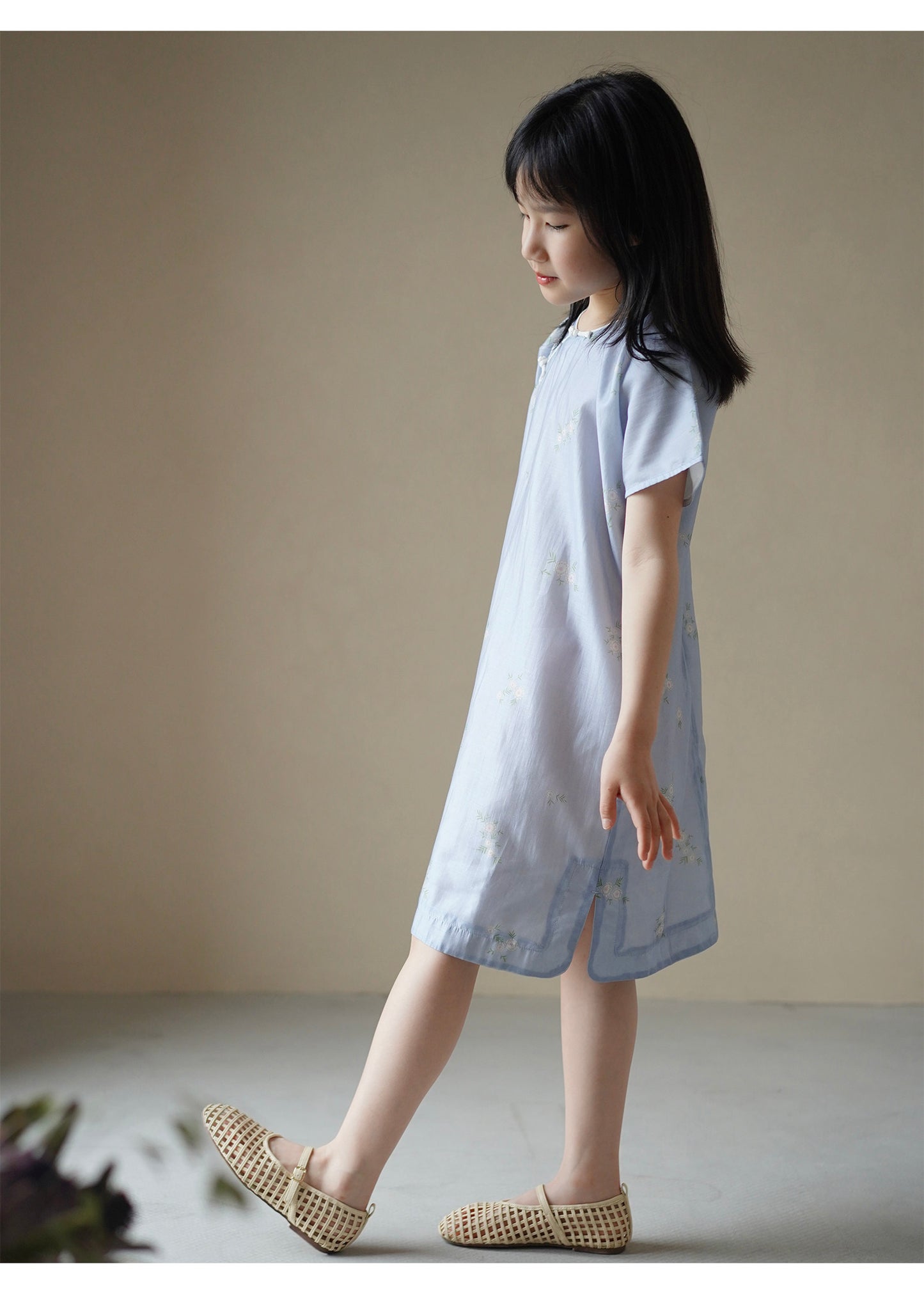 Young girl wearing a light blue dress standing against a plain background