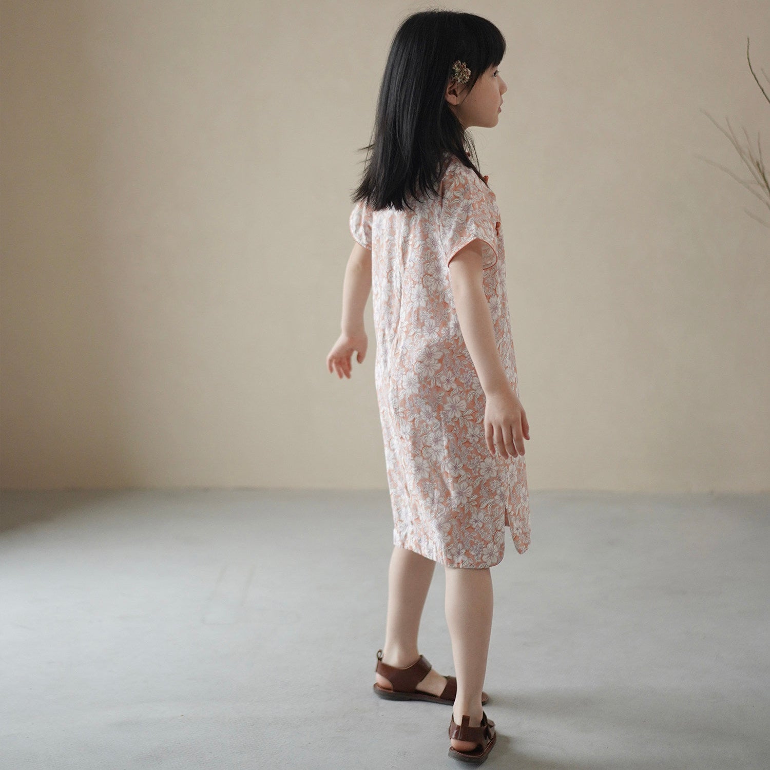 Young girl in a floral dress standing against a plain background