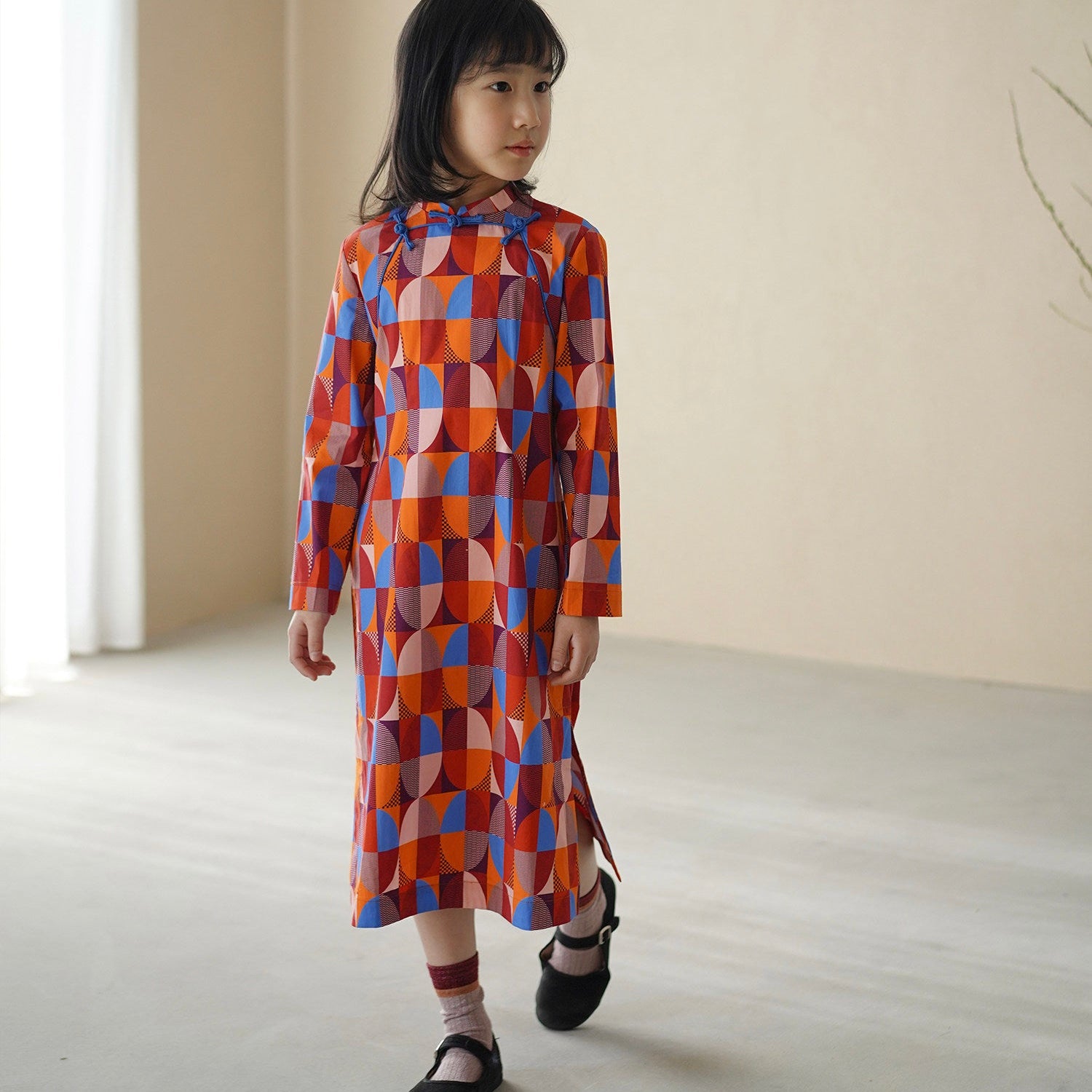 Child wearing a colorful geometric-patterned dress in a minimal indoor setting