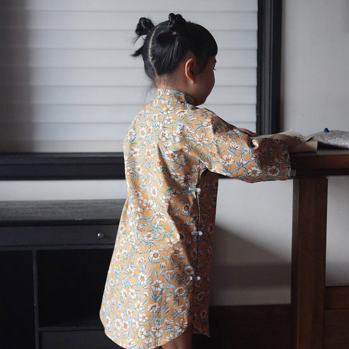 Child in a patterned dress standing at a table with a neutral background