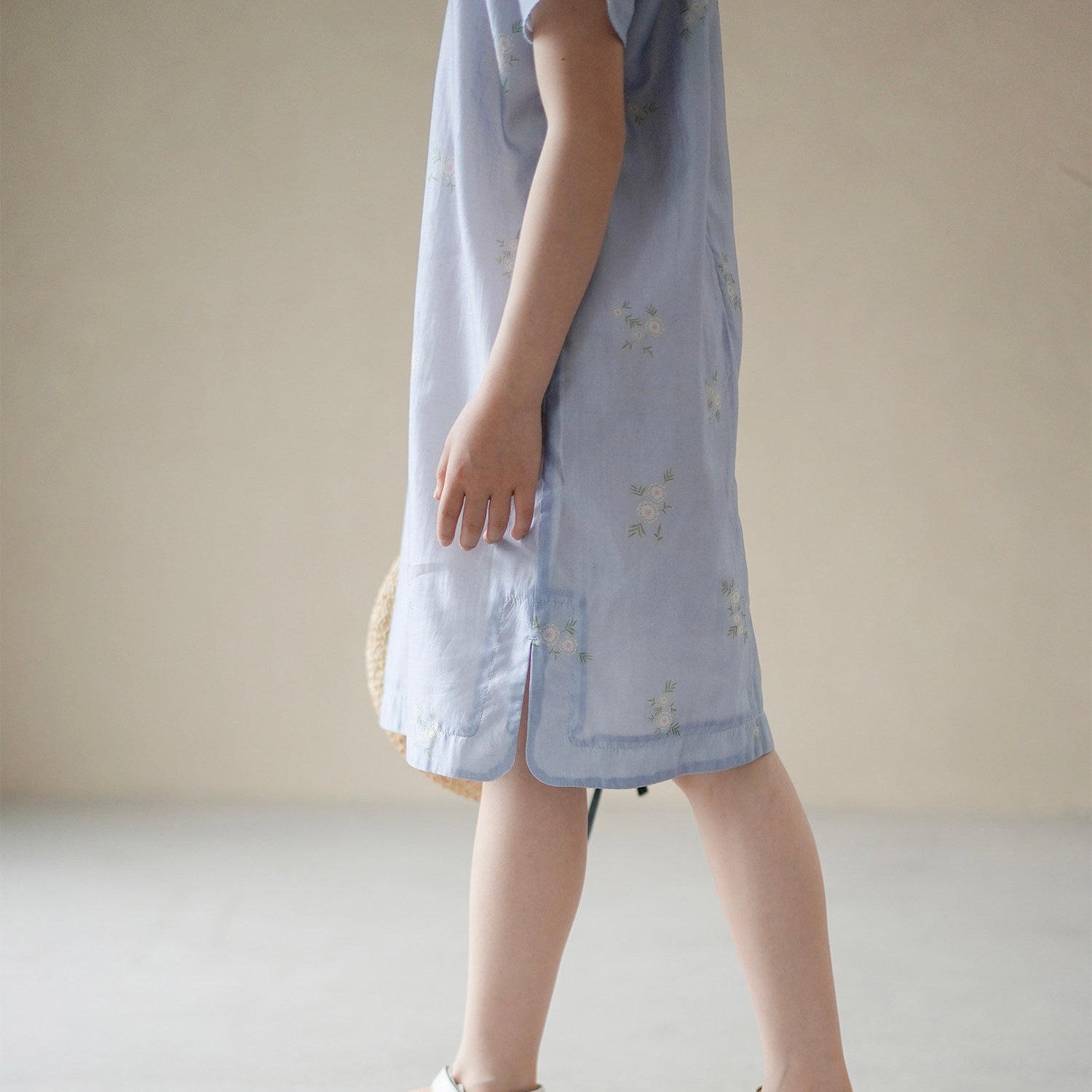 Person wearing a light blue dress with white sandals on a plain background