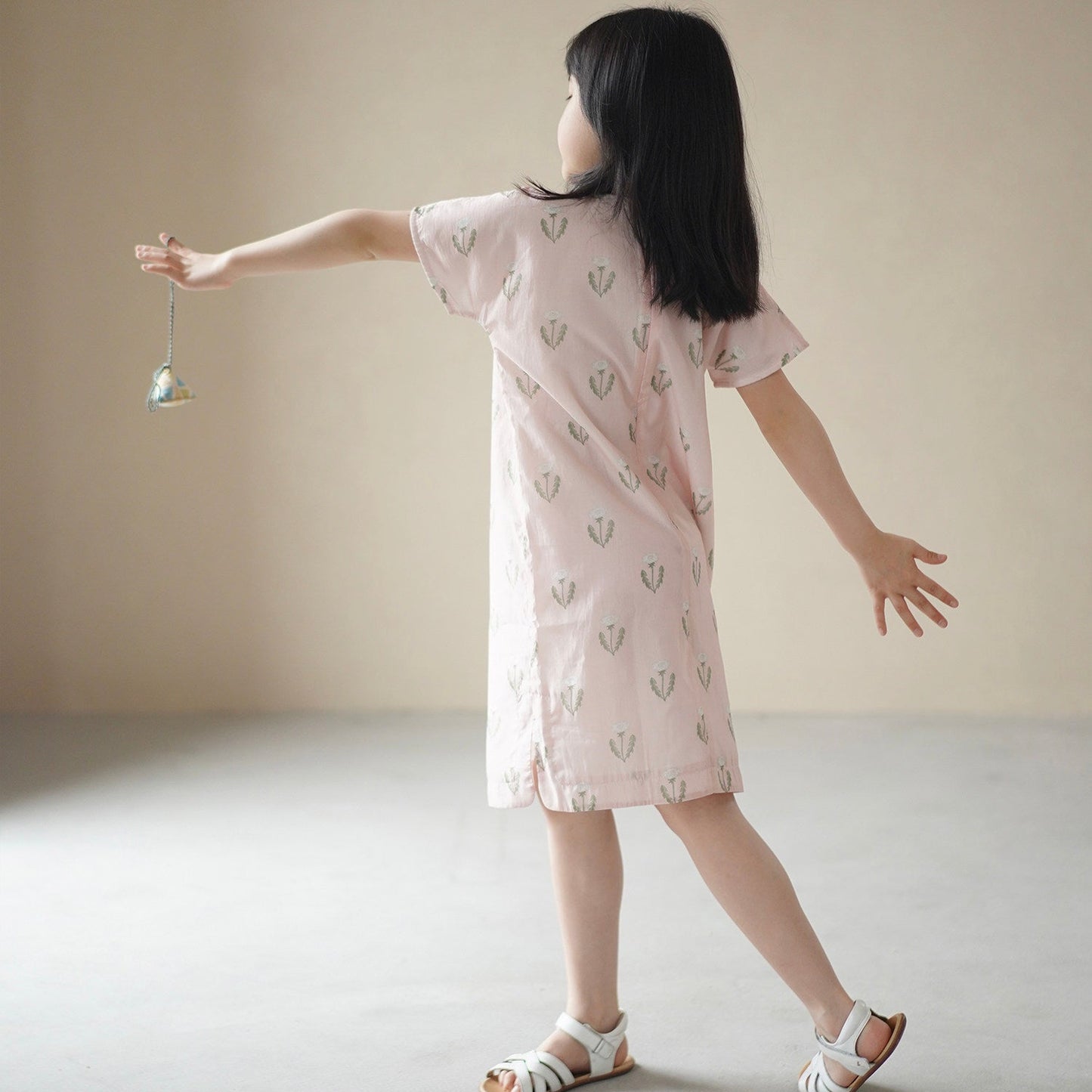 Child wearing a light pink dress with a subtle pattern, standing against a plain background.