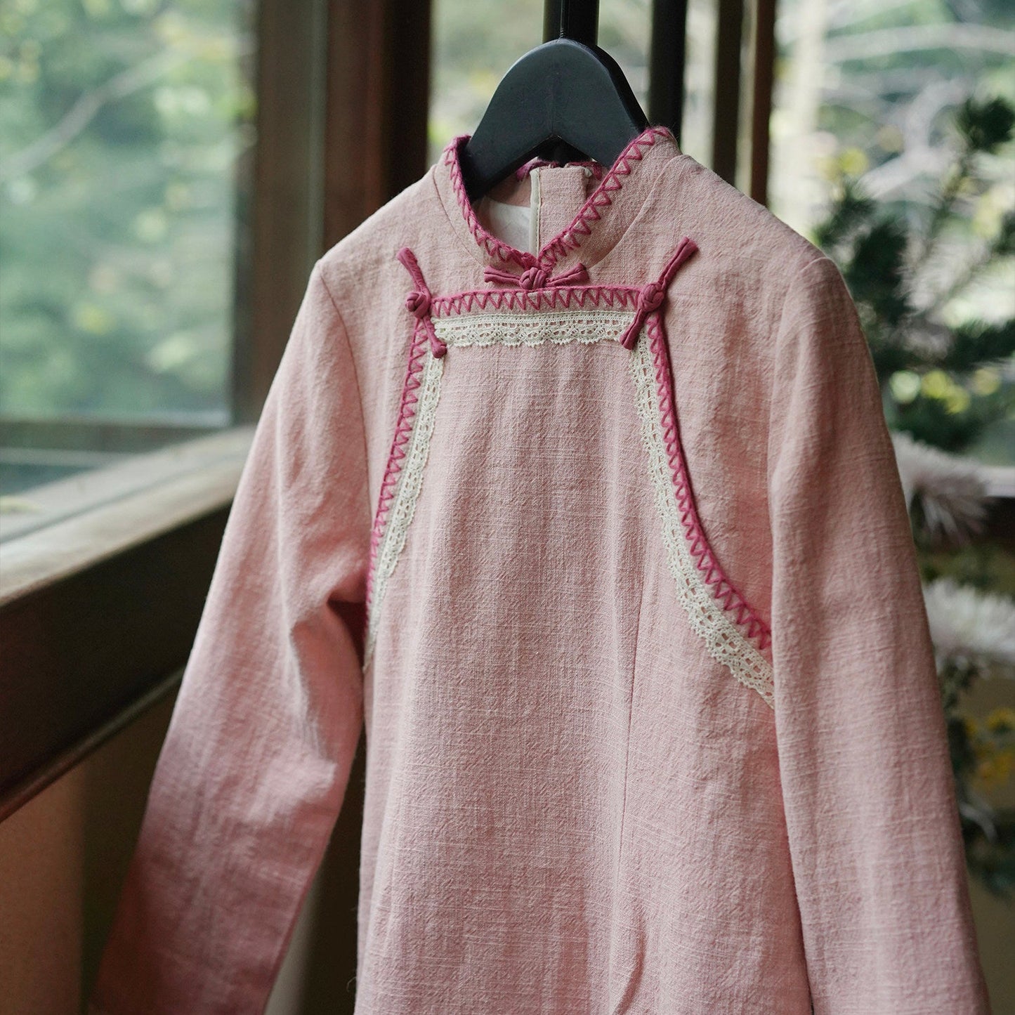 Pink dress with lace details on a hanger in front of a window