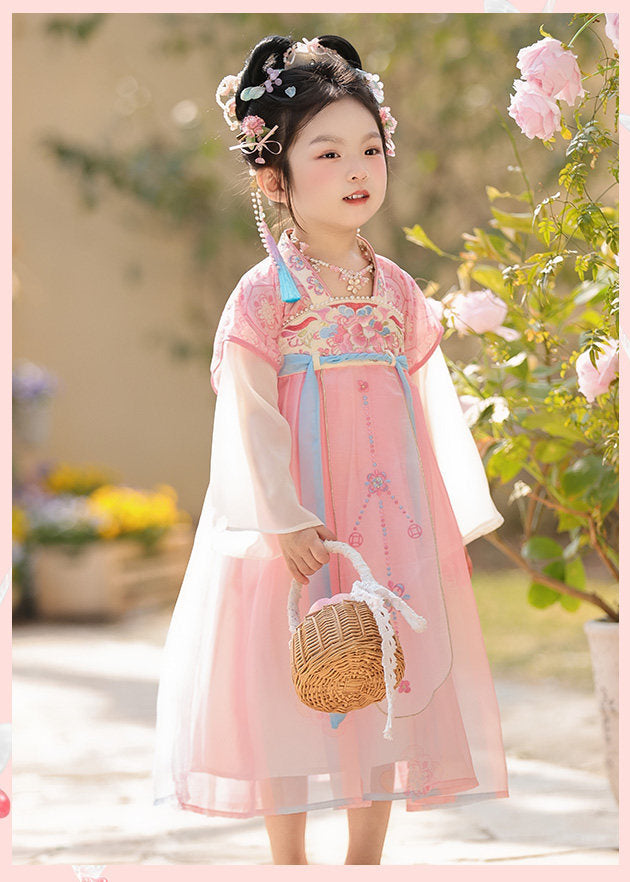 Child in traditional pink and white outfit with floral hair accessories, standing outdoors.