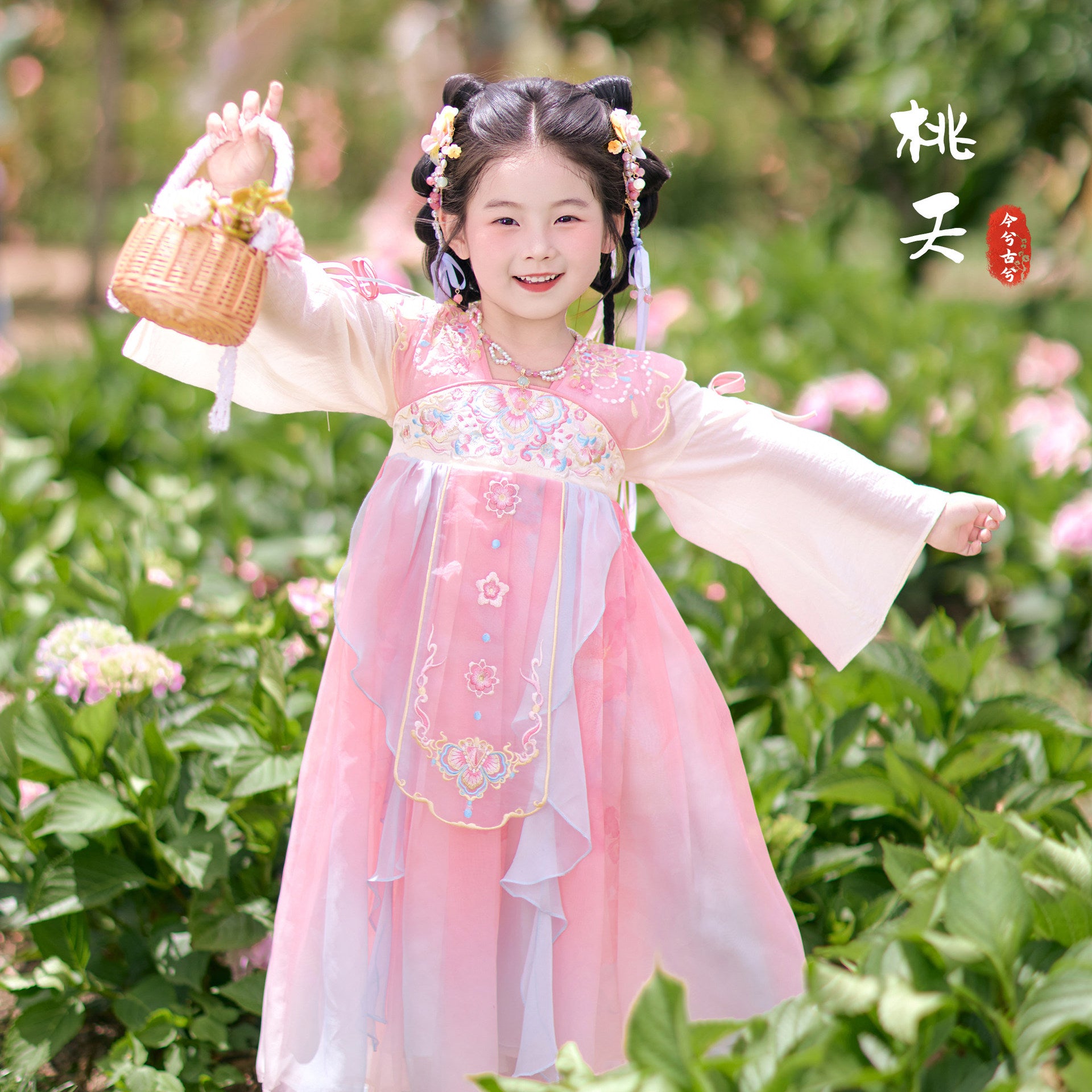 Child in traditional pink and white dress standing in a garden with flowers and greenery.