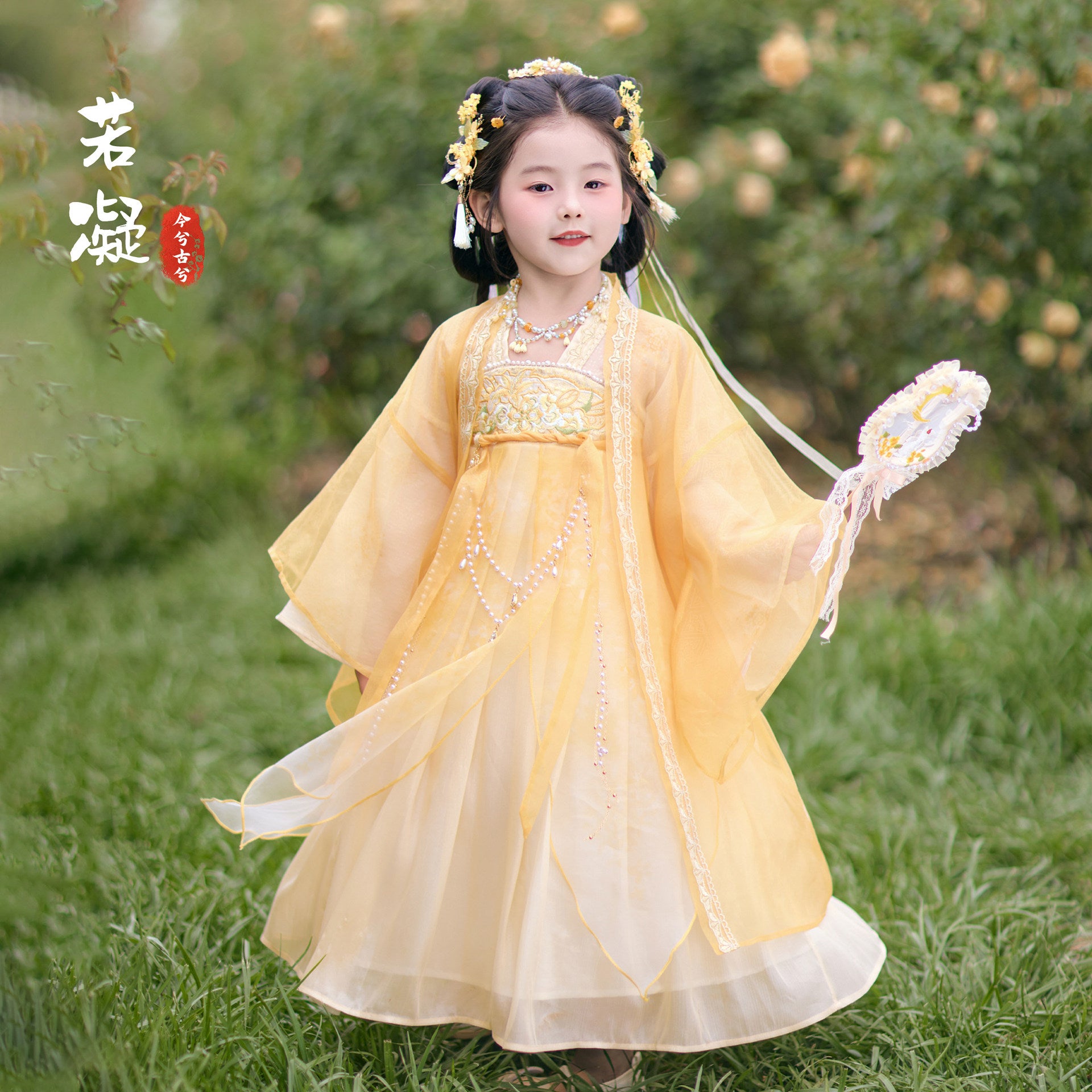 Child in a yellow traditional dress standing in a grassy area with blurred background