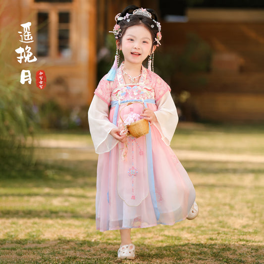 Child in traditional pink and white outfit holding a small round object outdoors.