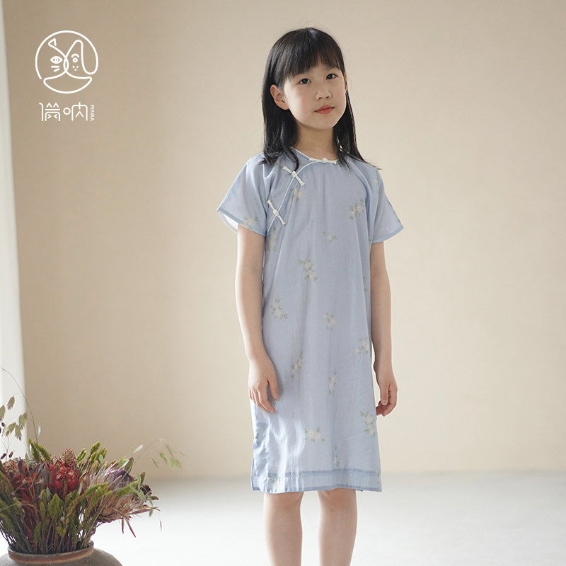 Young girl wearing a light blue dress with a subtle pattern, standing against a plain background.