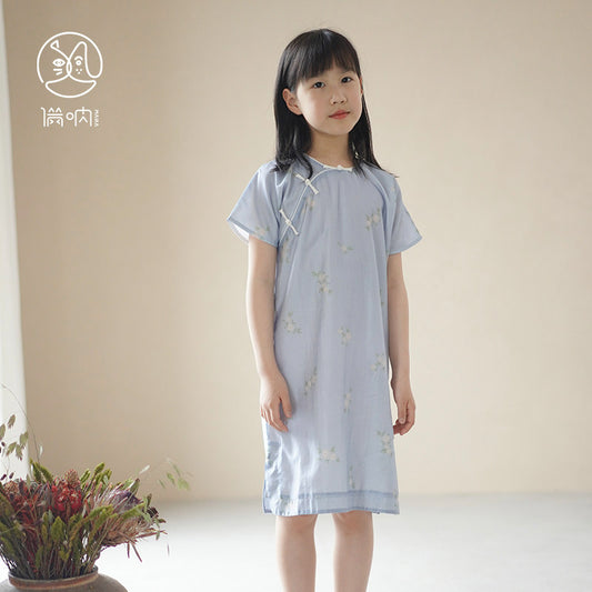 Young girl wearing a light blue dress with a subtle pattern, standing against a plain background.