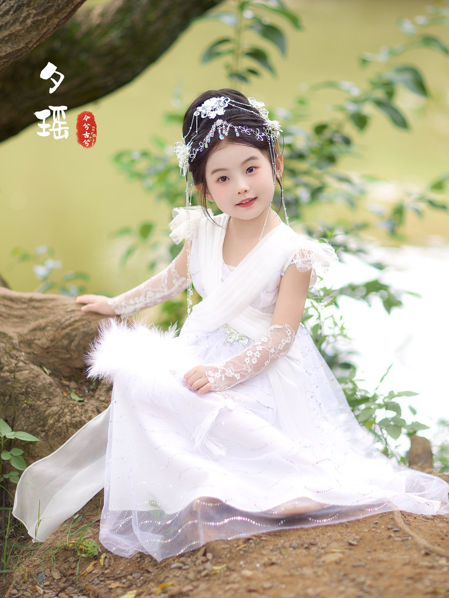 Young girl in a white dress sitting on a tree branch with greenery in the background