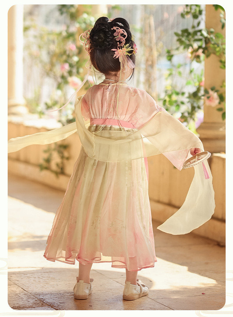Child wearing a traditional outfit with floral hair accessories in a softly lit room.