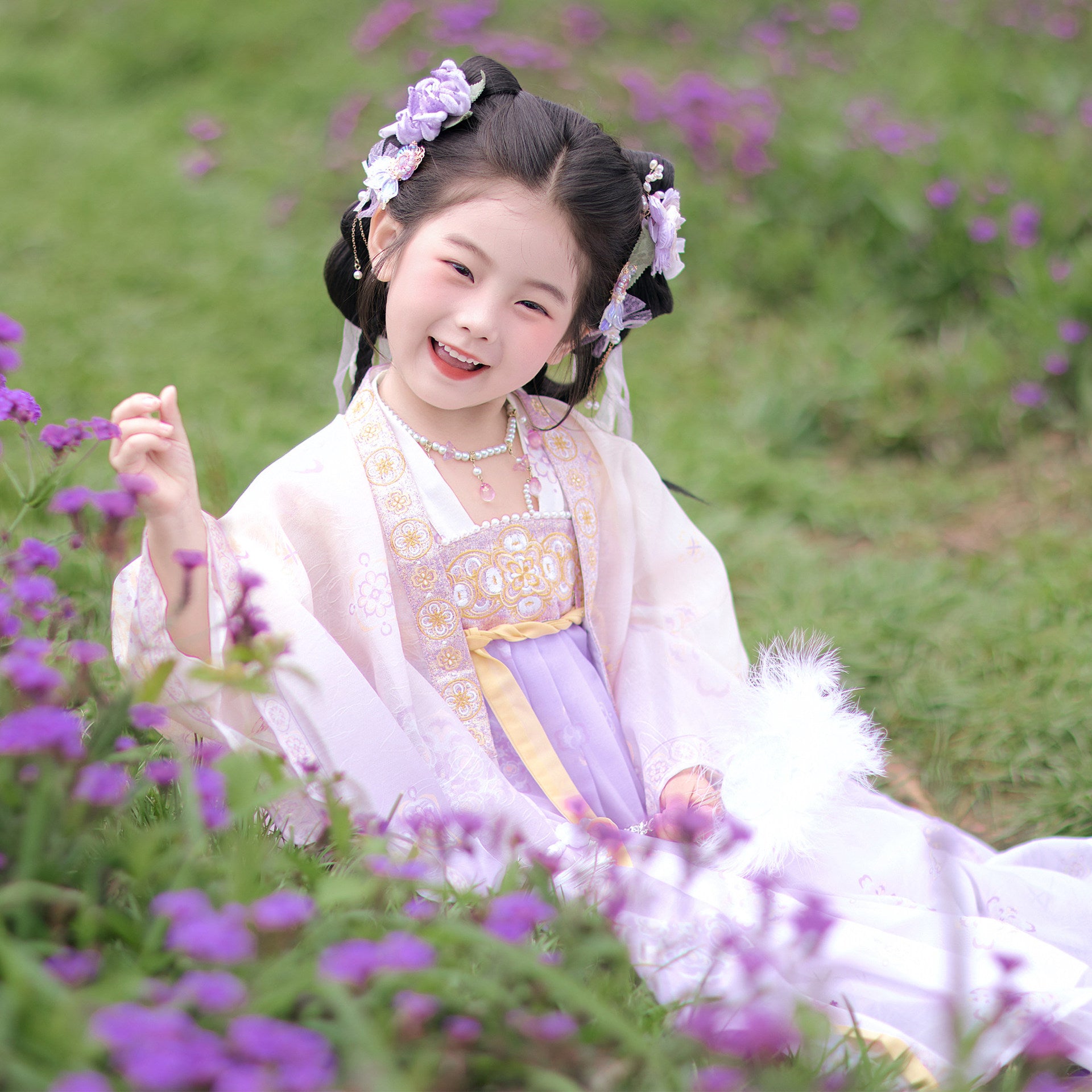 Young girl in traditional attire sitting among purple flowers
