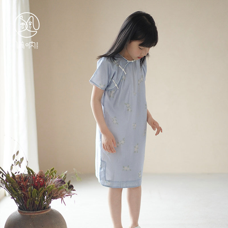 Young girl in a light blue dress standing in a room with a vase of flowers.