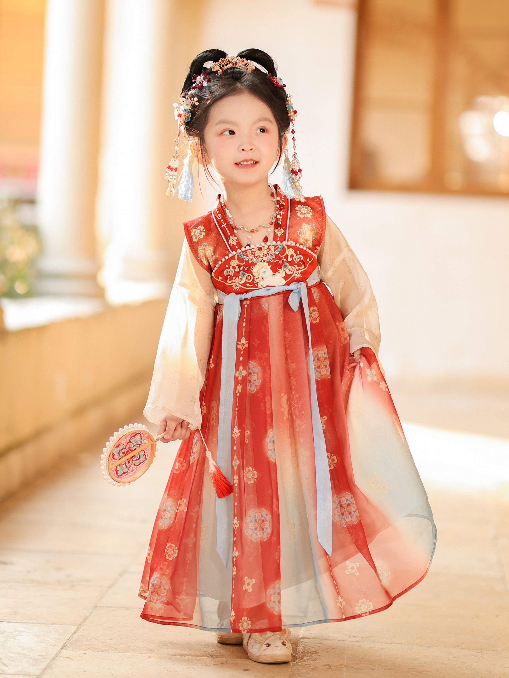 Child wearing a traditional red and white dress with floral patterns indoors.