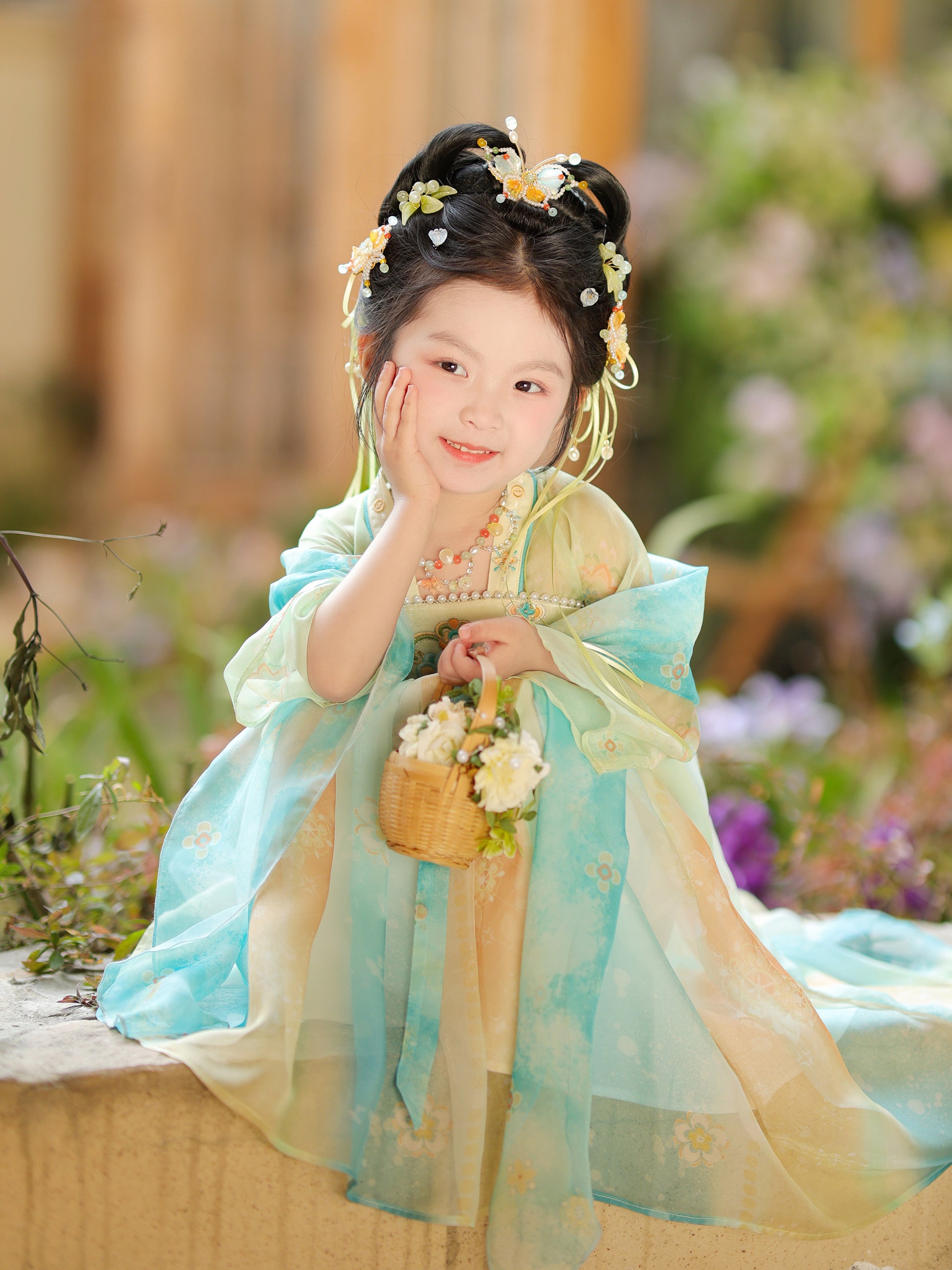 Child in traditional attire with floral hair accessories and a basket of flowers, outdoors.
