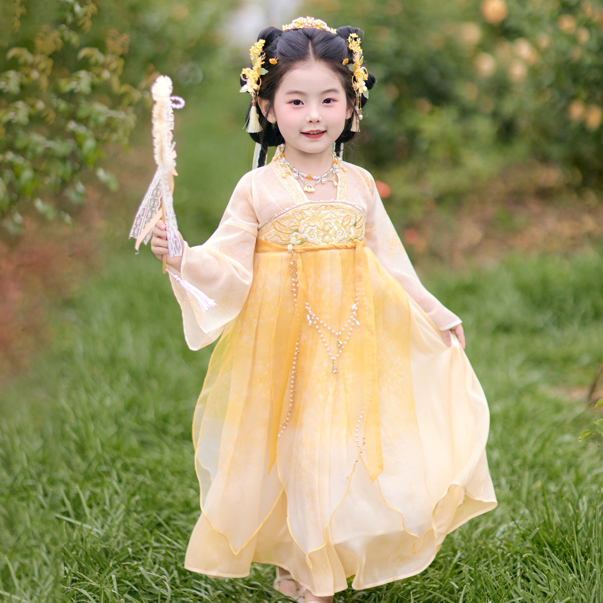 Child in a traditional yellow dress holding a fan outdoors