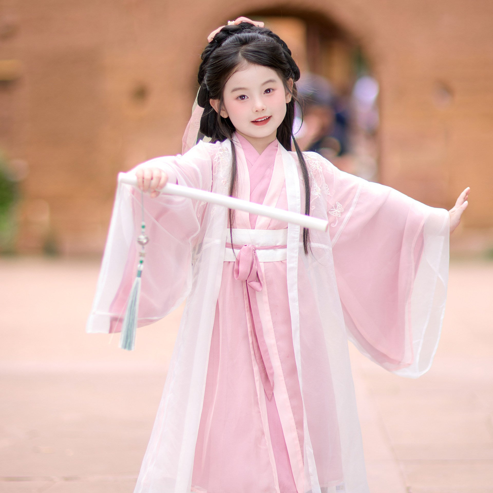 Child in a traditional pink and white outfit holding a staff against a blurred background