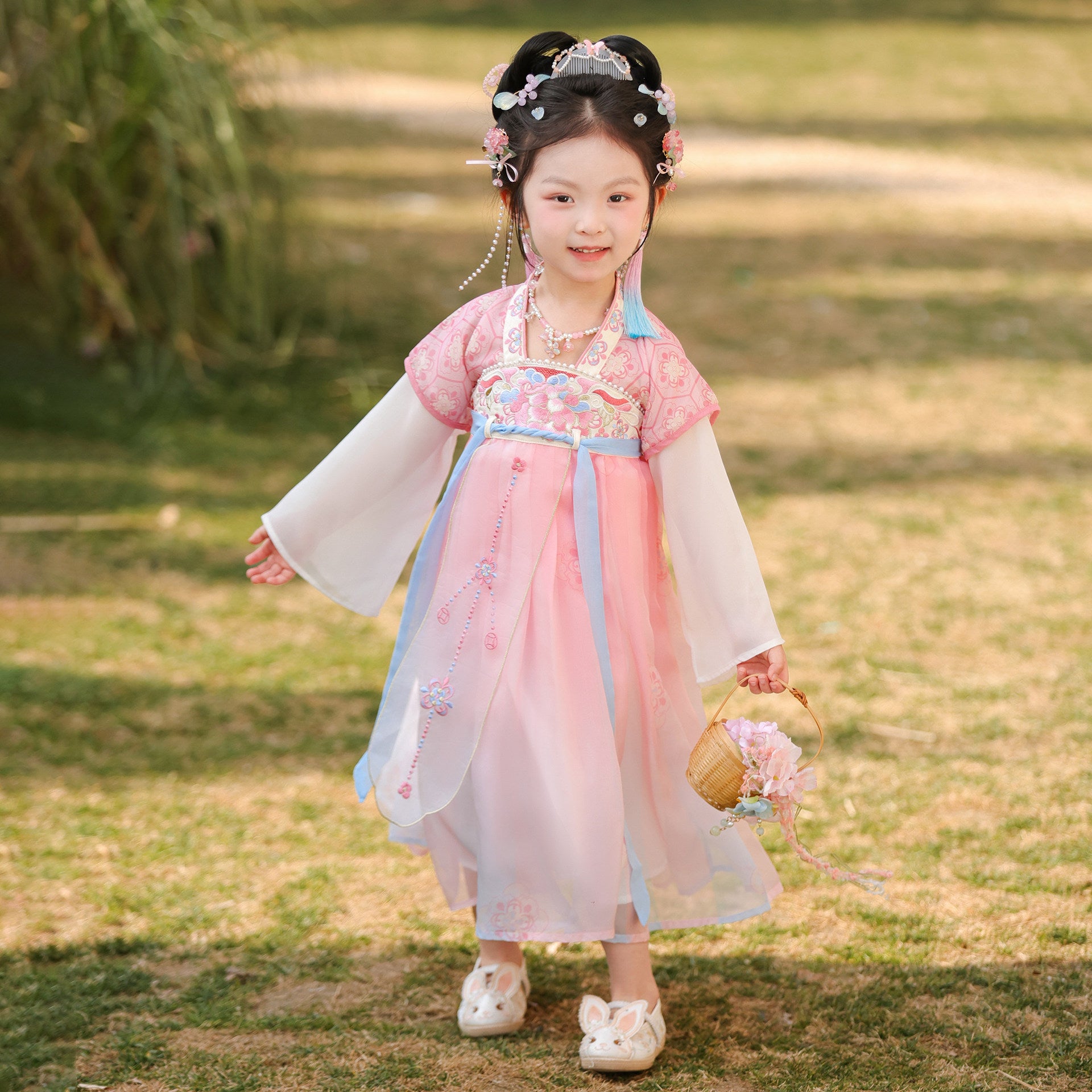 Young girl in traditional Chinese attire standing outdoors on grass.