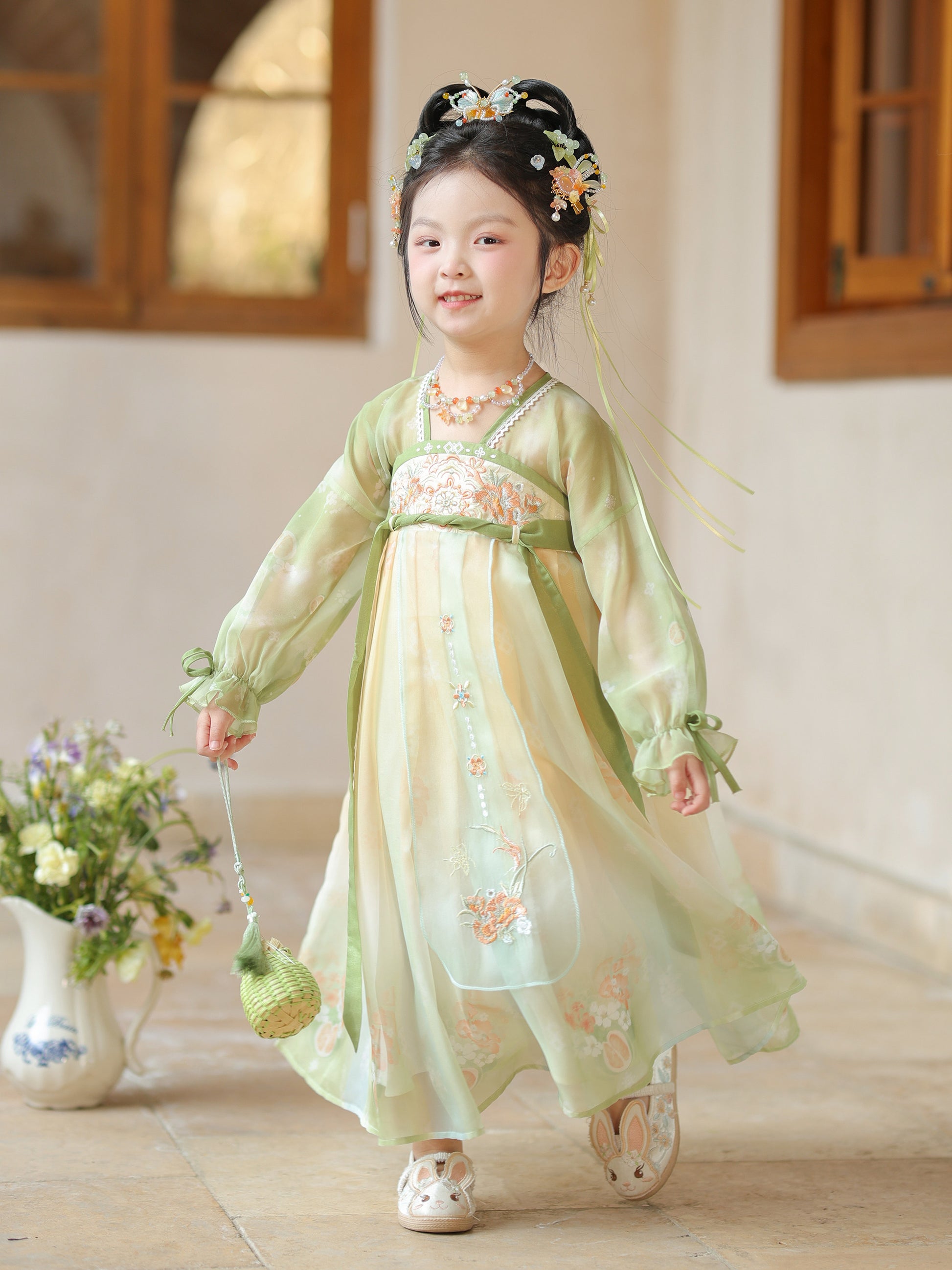 Young girl in a traditional light green dress with floral patterns indoors.