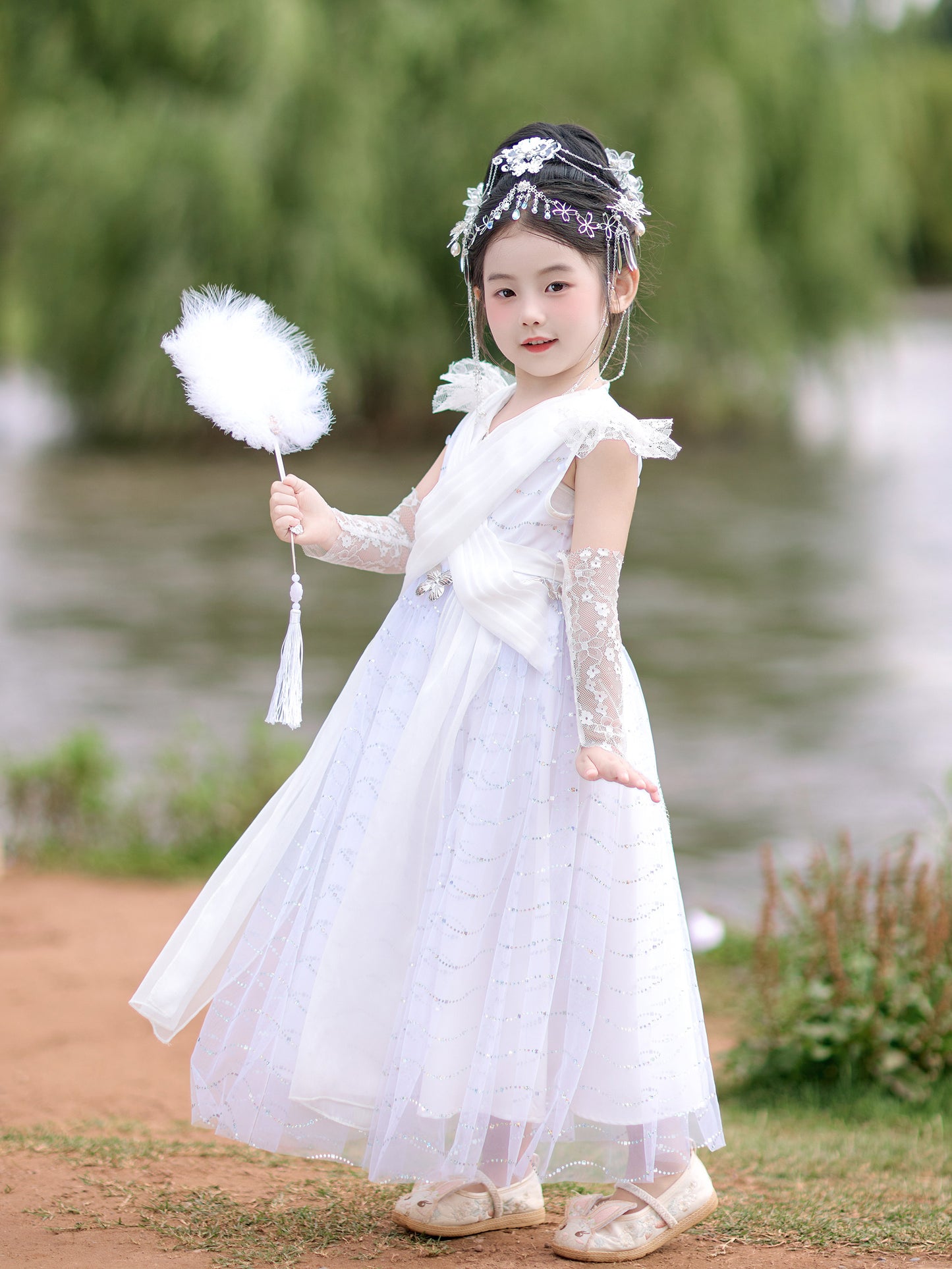 Young girl in a white dress holding a white flower by a body of water.