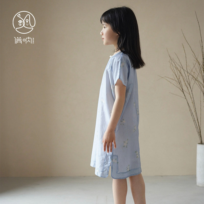 Young girl wearing a light blue dress with star patterns against a beige wall.