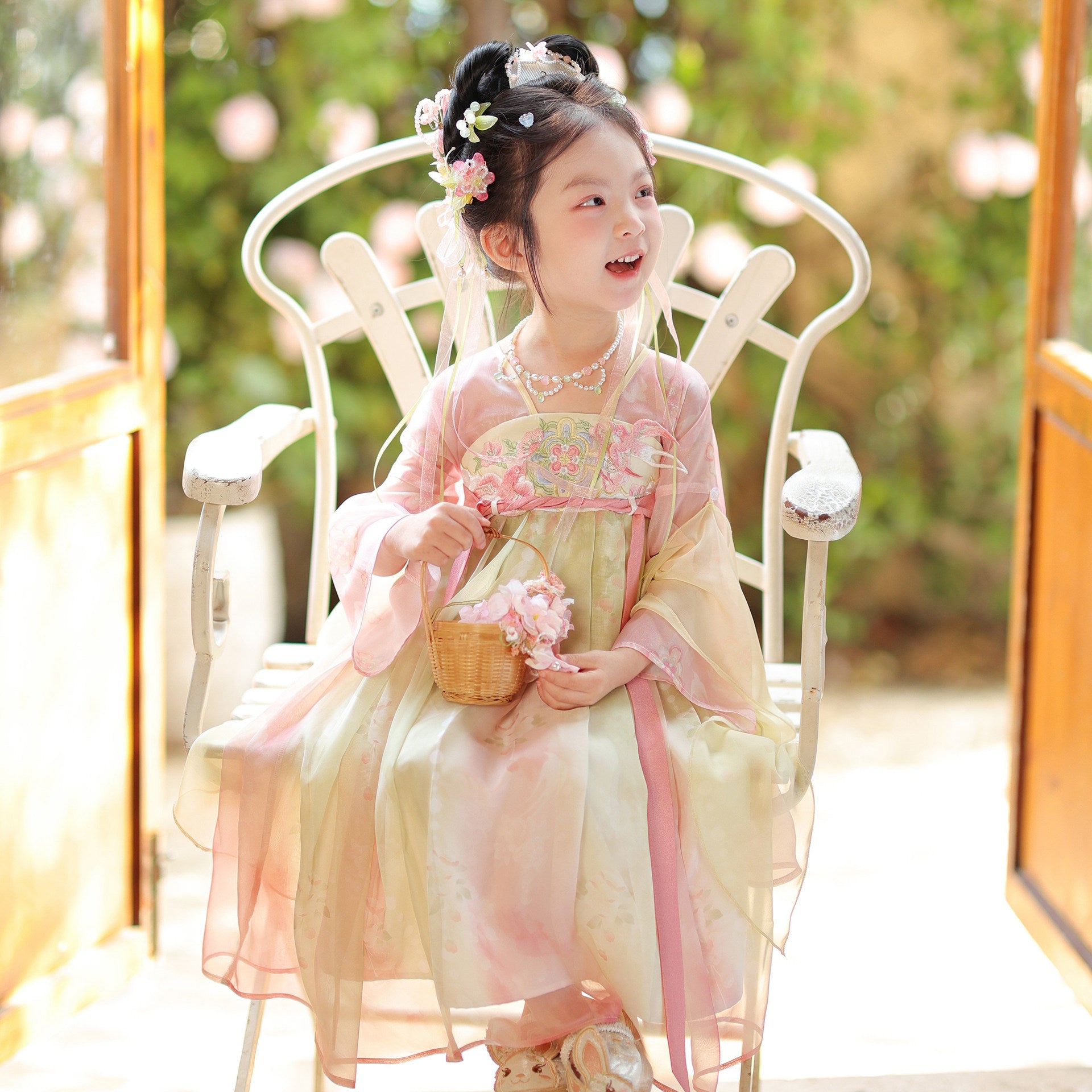 Young girl in a traditional outfit sitting on a white chair outdoors.