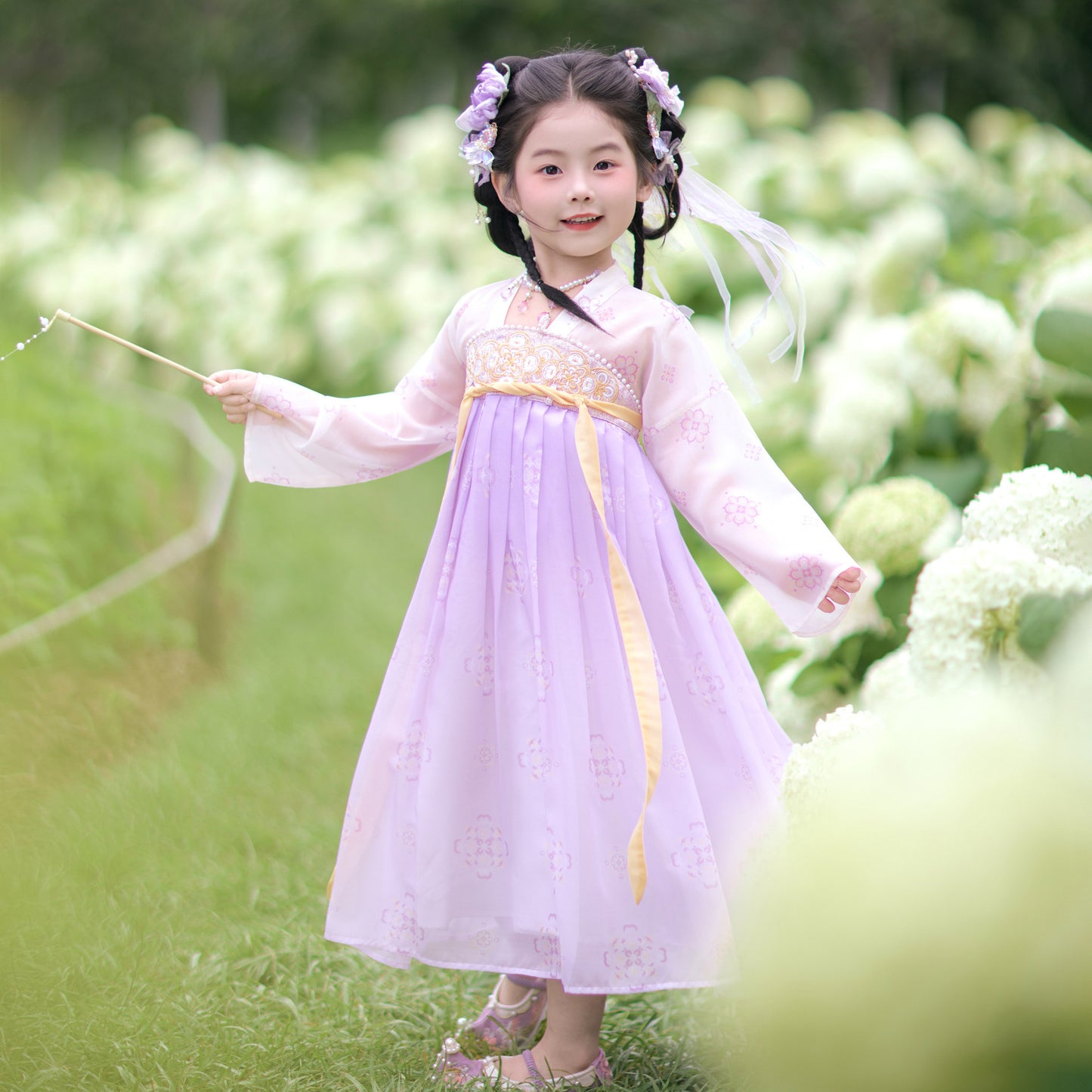 Young girl in a traditional outfit standing in a garden with white flowers.