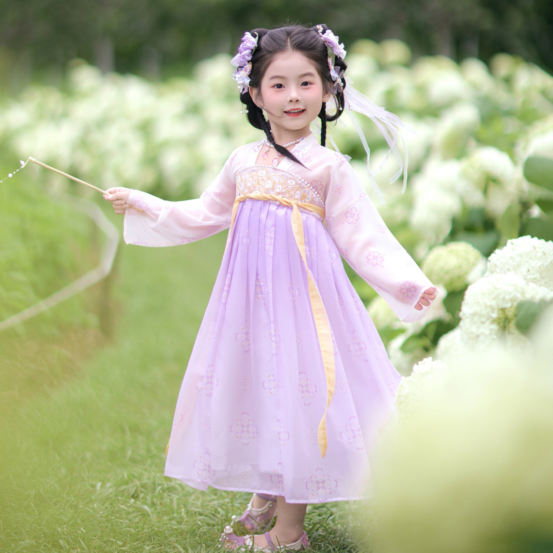 Young girl in a traditional outfit standing in a garden with white flowers.