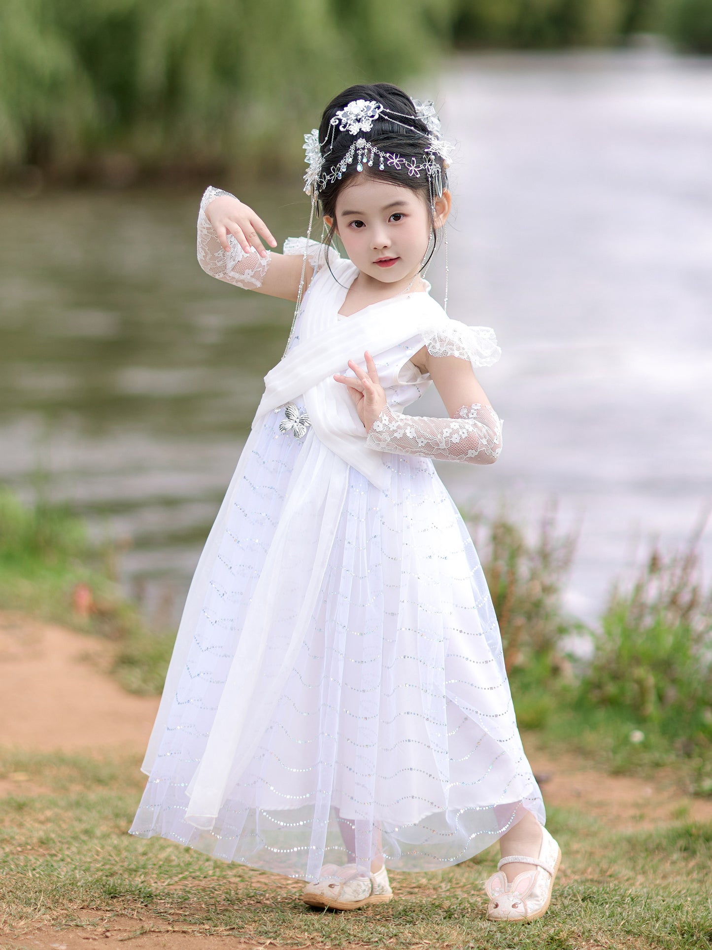 Young girl in a white dress standing outdoors near a body of water.
