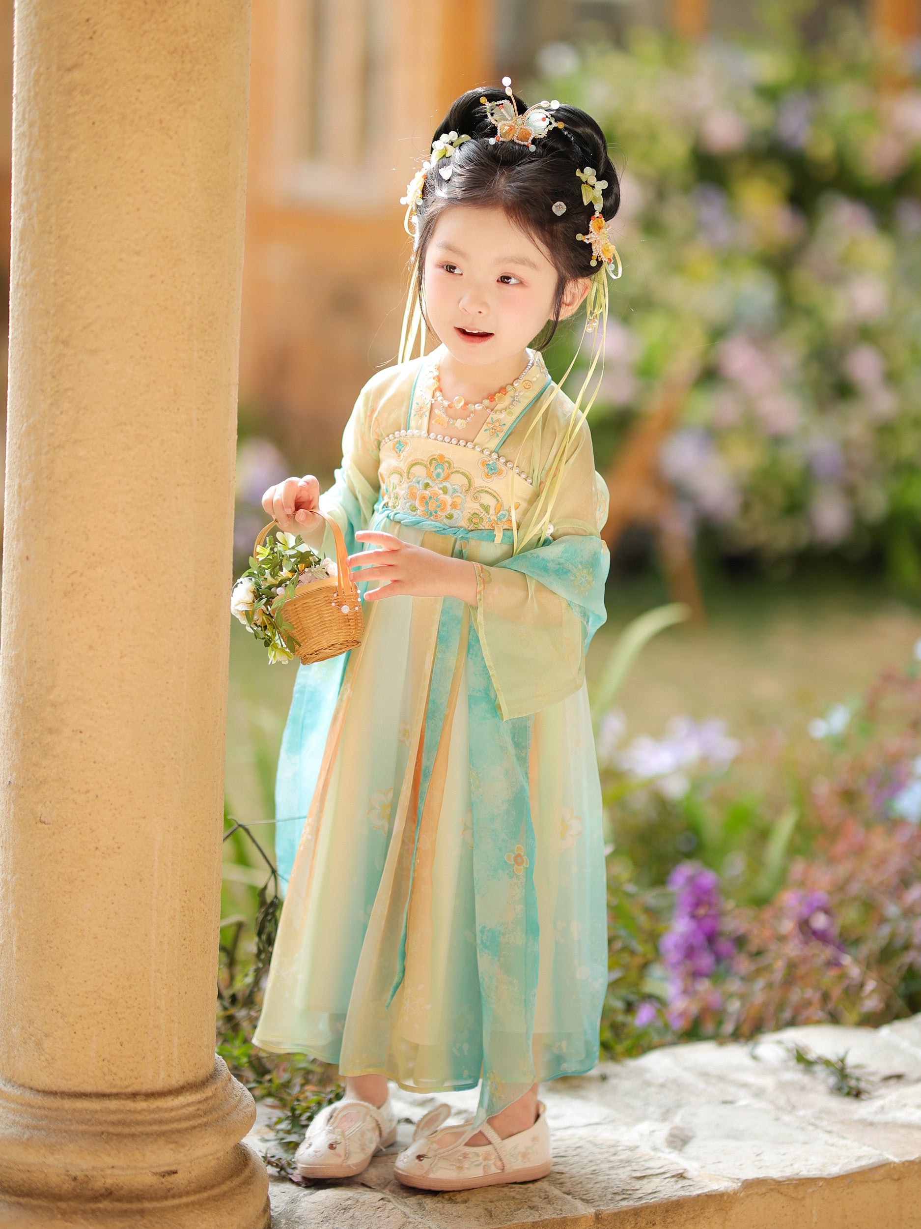 Child in traditional outfit holding a basket in a garden setting
