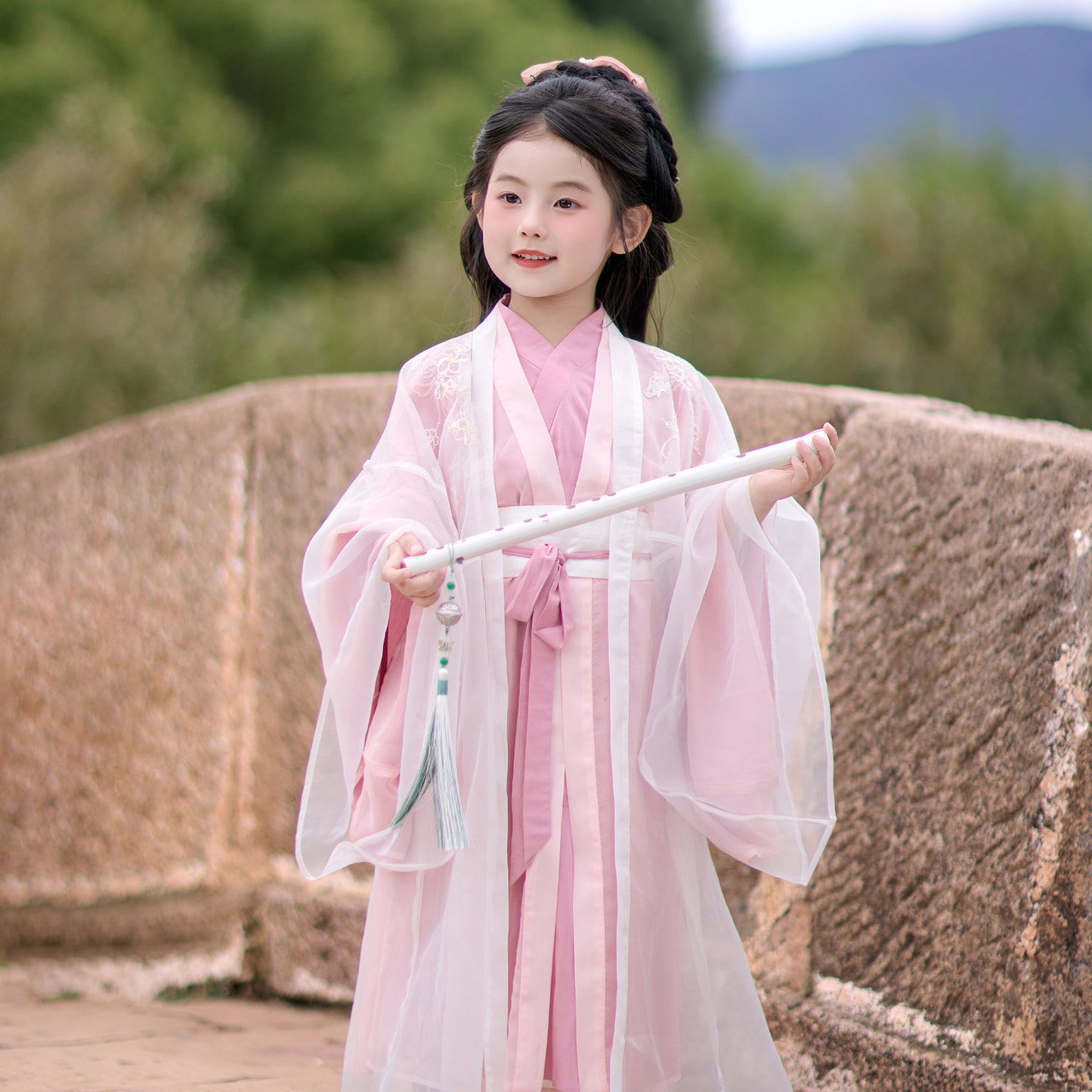 Child in traditional pink and white outfit holding a sword outdoors.