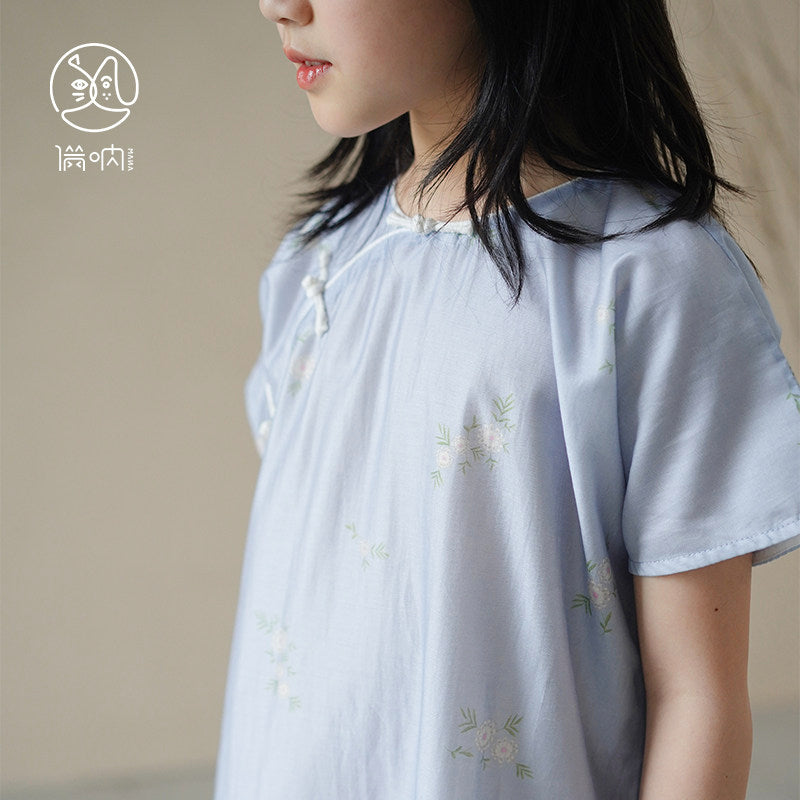 Child wearing a light blue dress with floral embroidery on a plain background