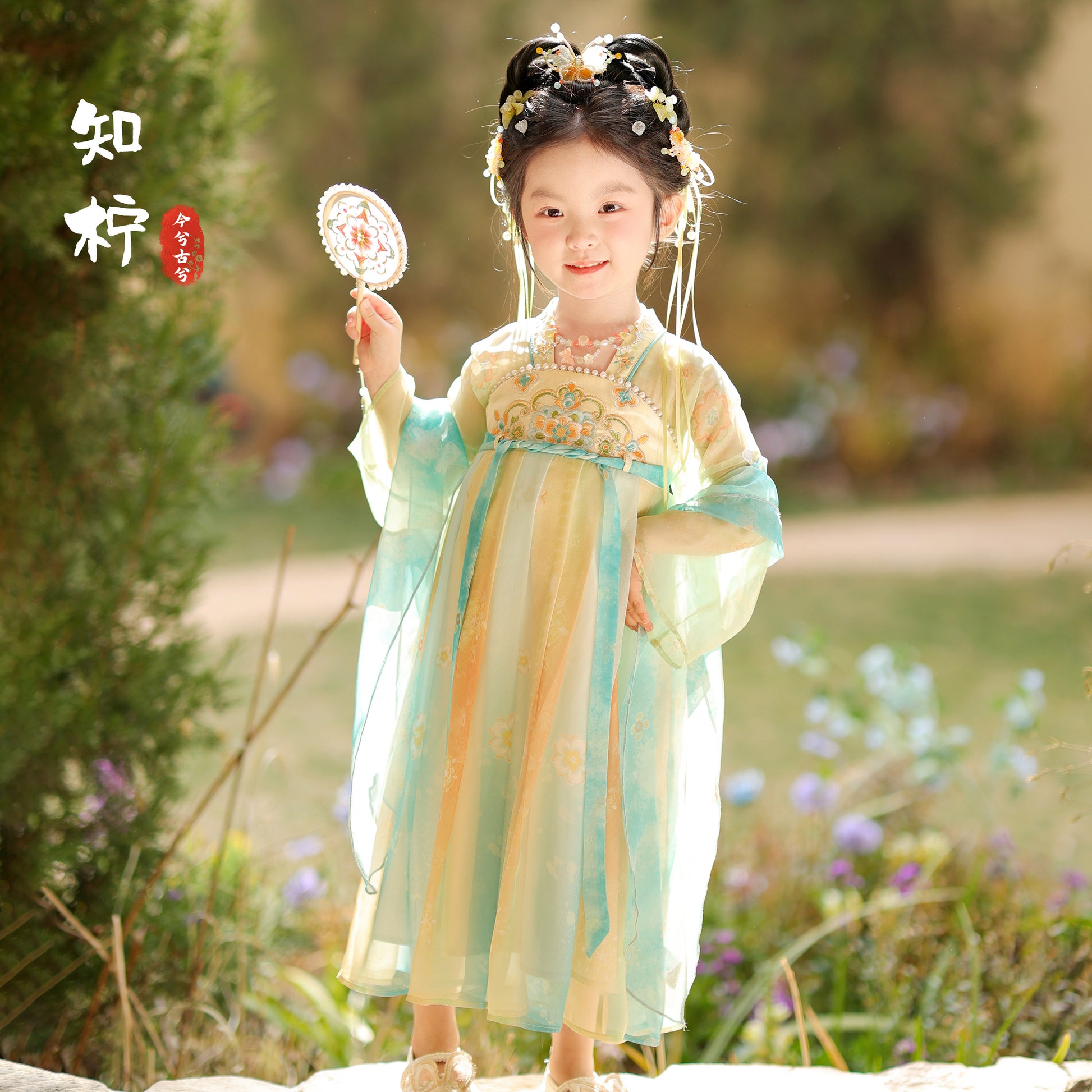 Child in traditional outfit holding a decorative item in a natural setting