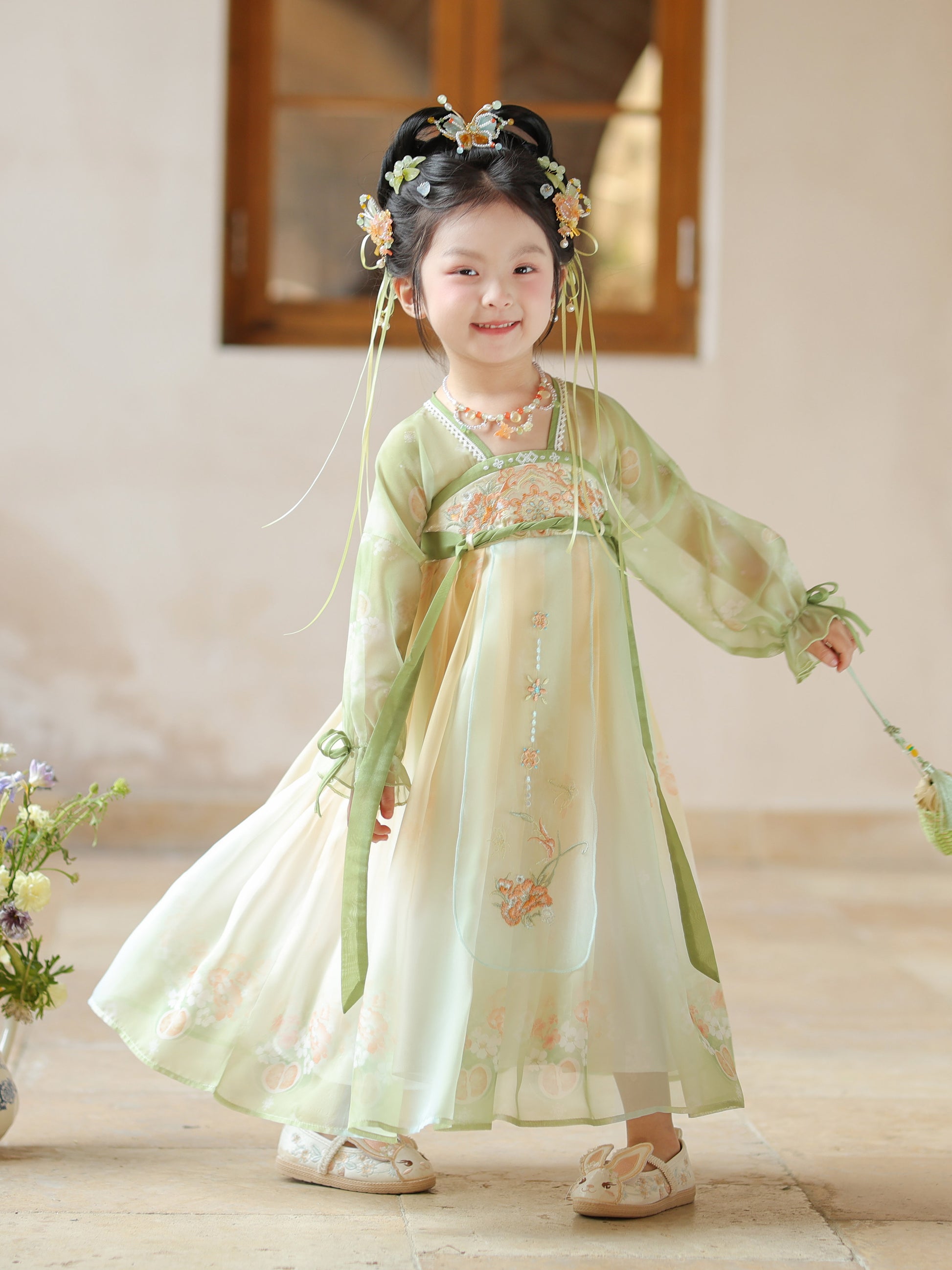 Child wearing a traditional green and white dress with floral decorations indoors.