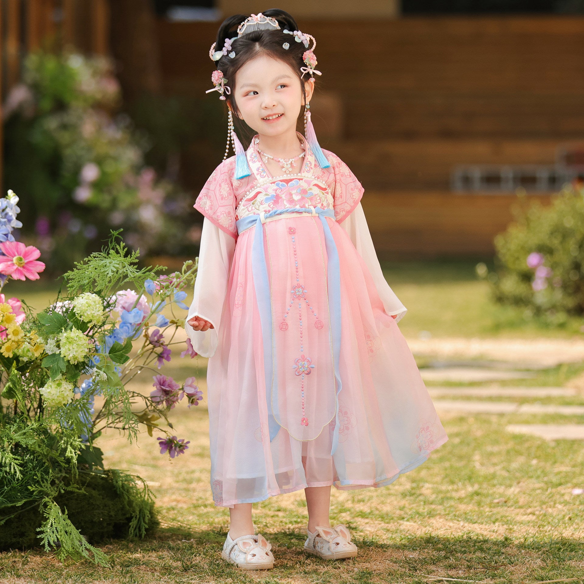 Young girl in a traditional outfit standing outdoors with flowers and greenery.