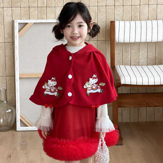 Young girl wearing a red dress with cat designs in a room with wooden floor and tiled wall.
