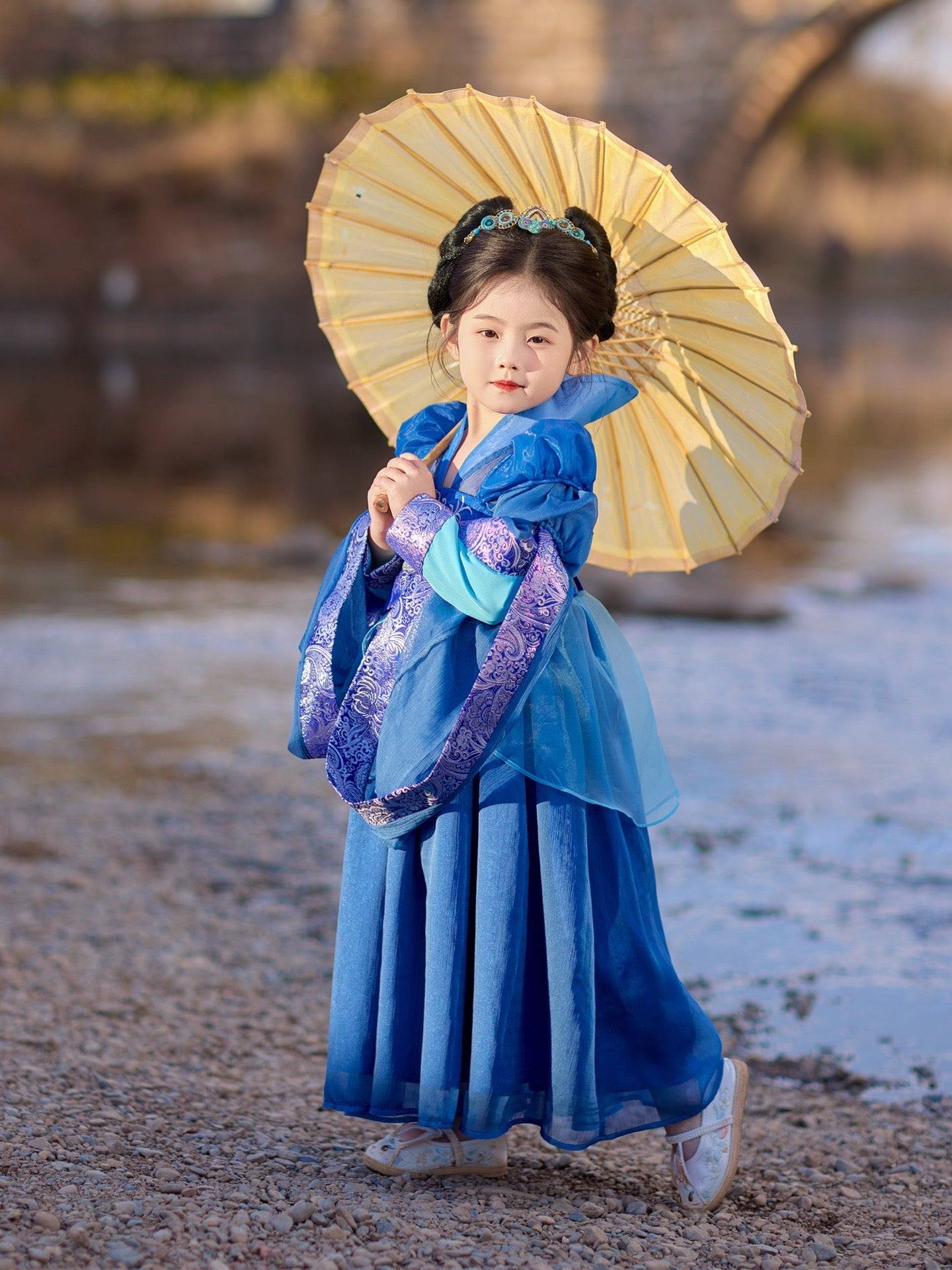 Child in traditional blue dress holding a yellow umbrella outdoors