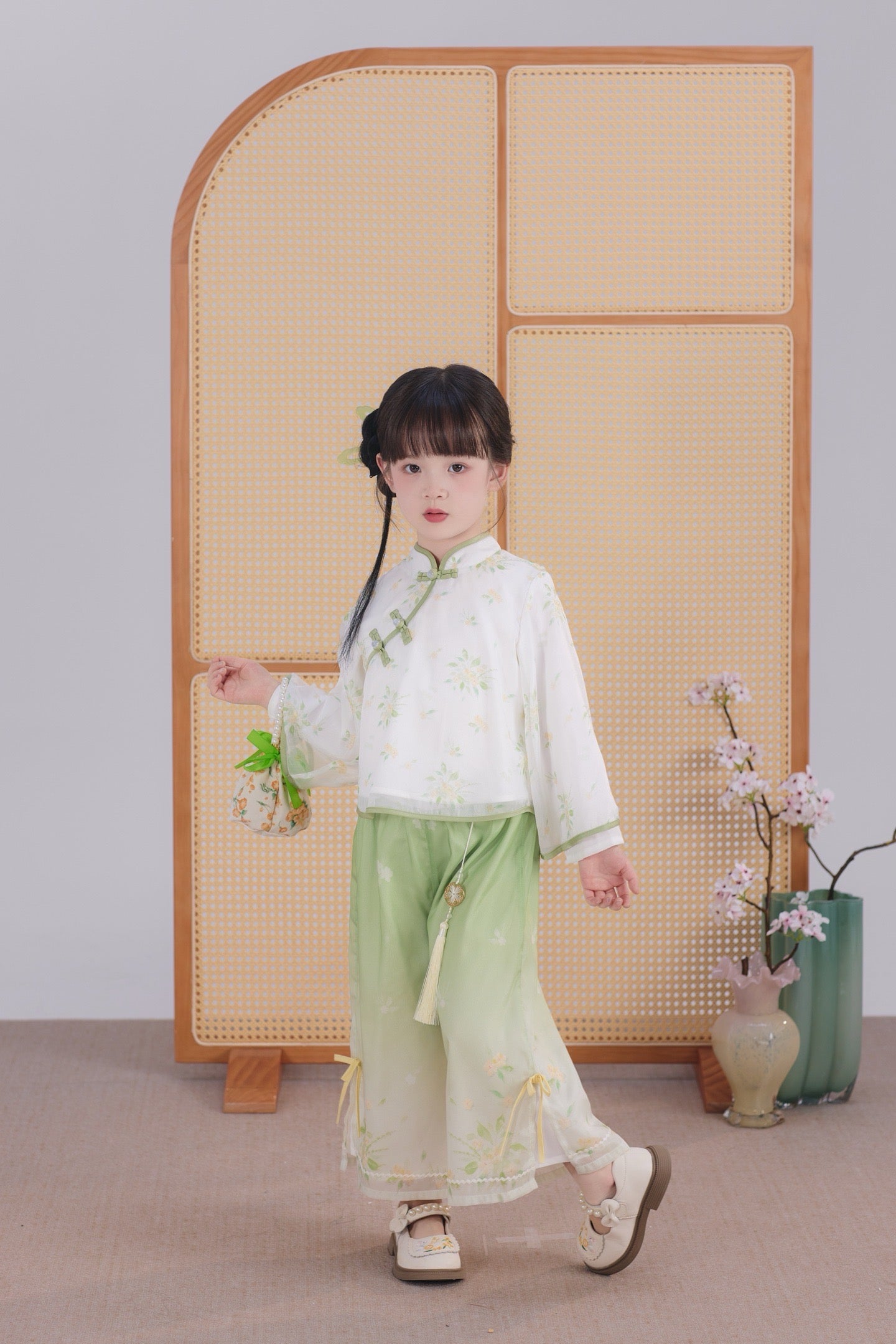 Child in traditional outfit standing in front of a wooden screen with floral decorations.