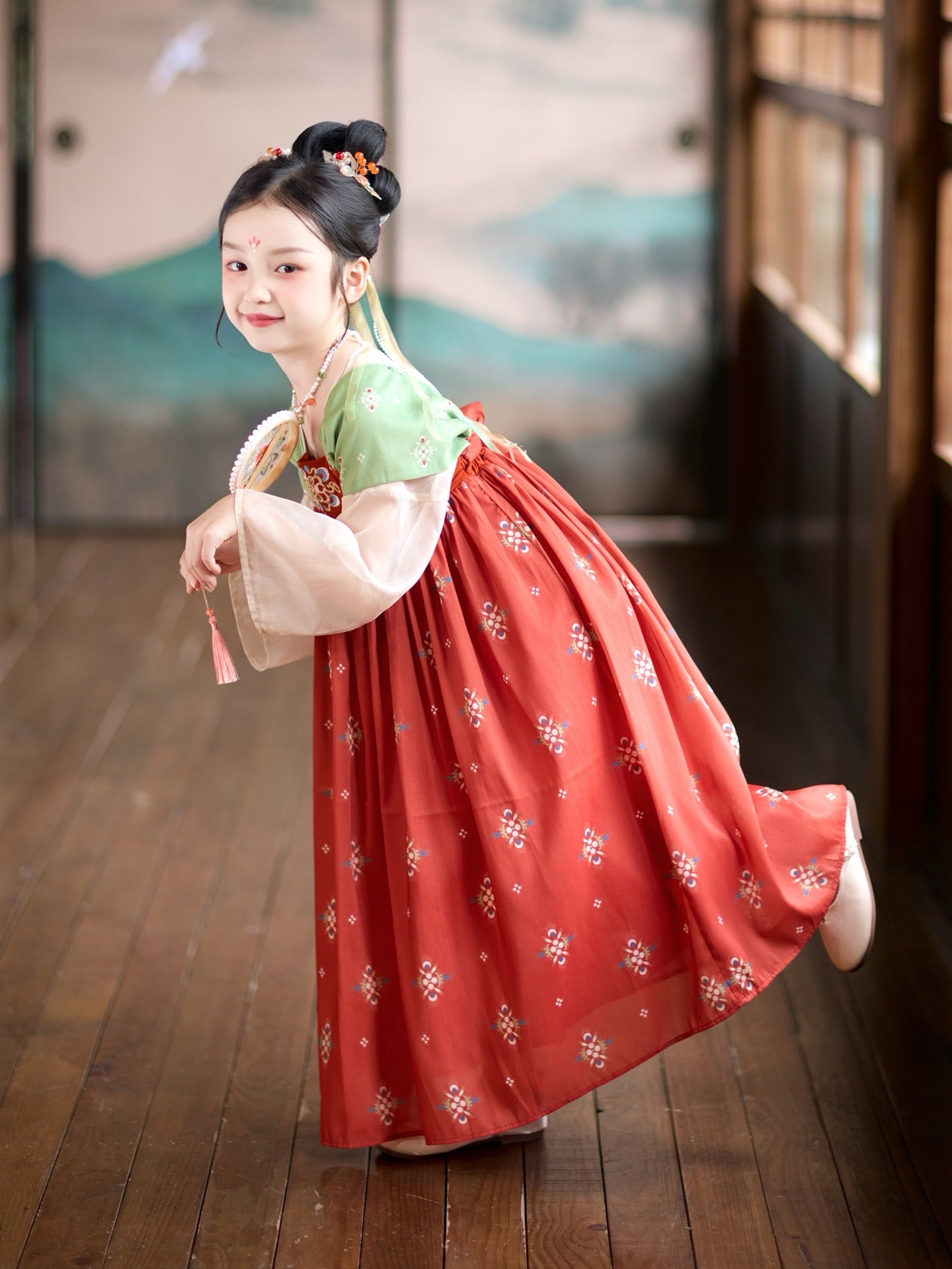 Child in traditional red and green dress on wooden floor